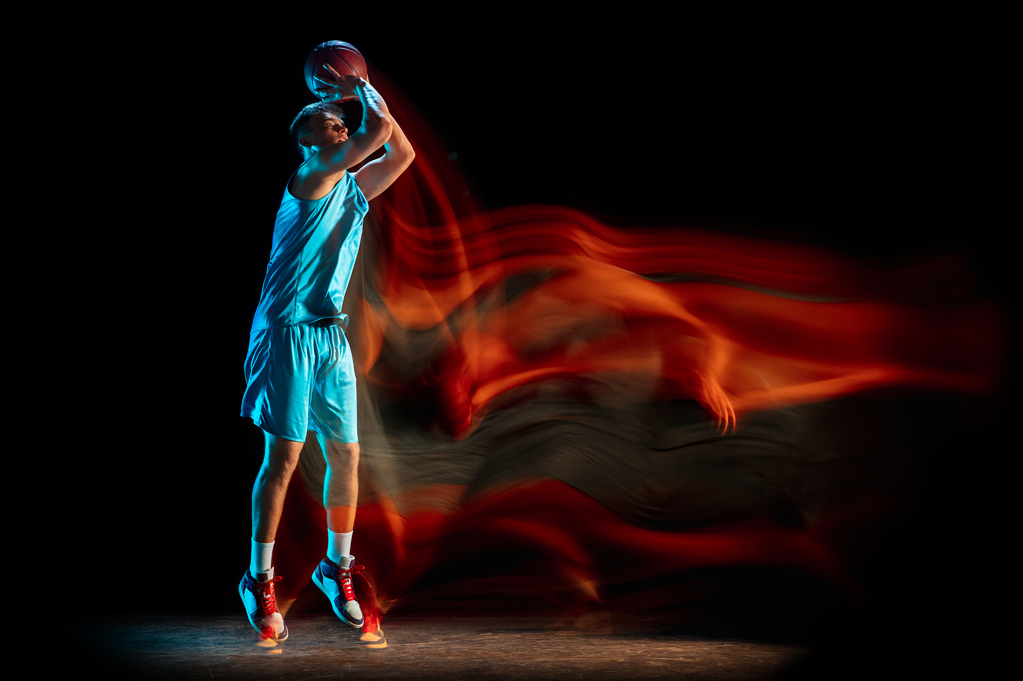 Male basketball player playing basketball isolated over dark studio background in mixed light.